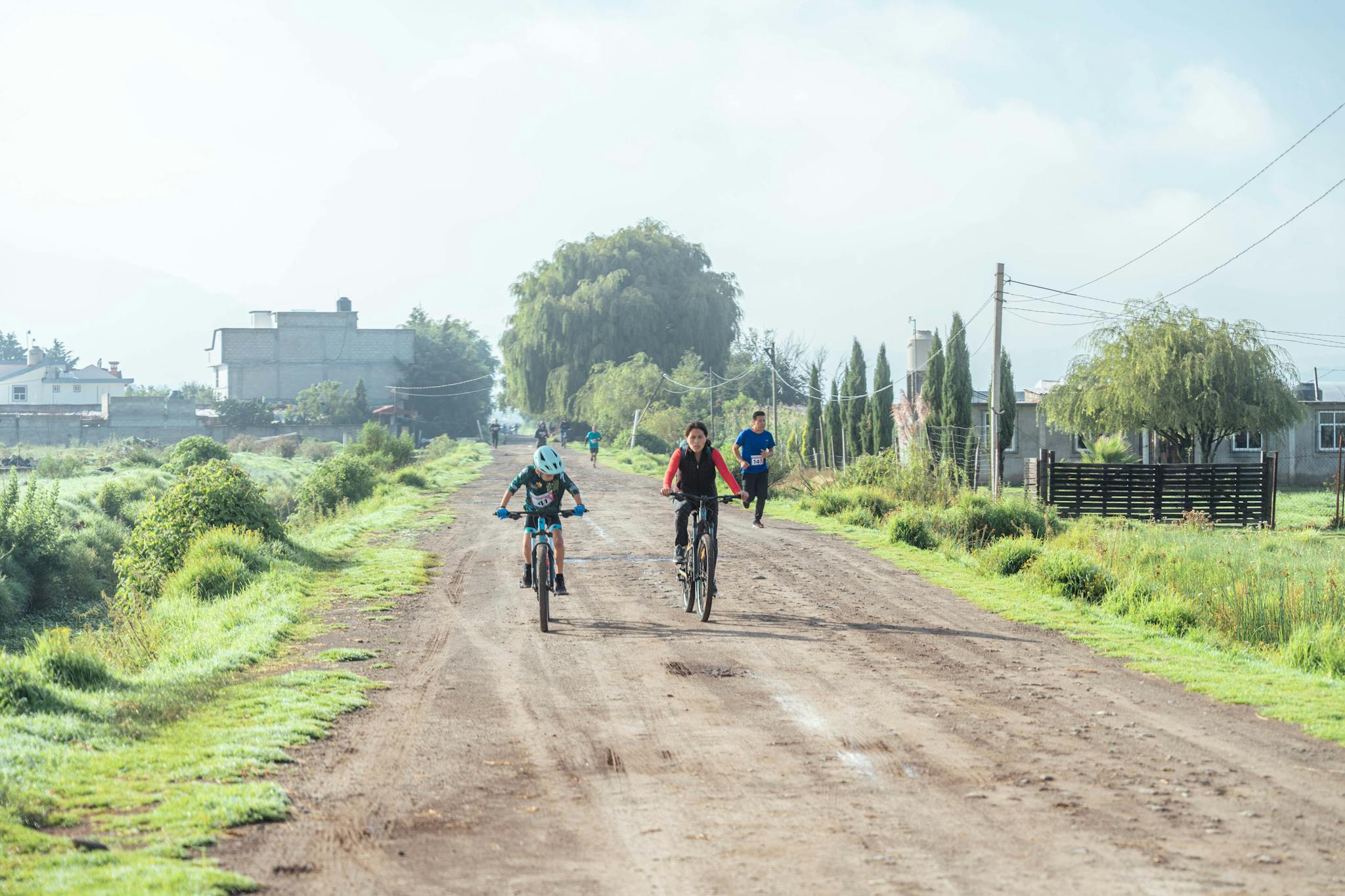 A group of cyclists enjoying a morning ride on a rural dirt road surrounded by greenery.